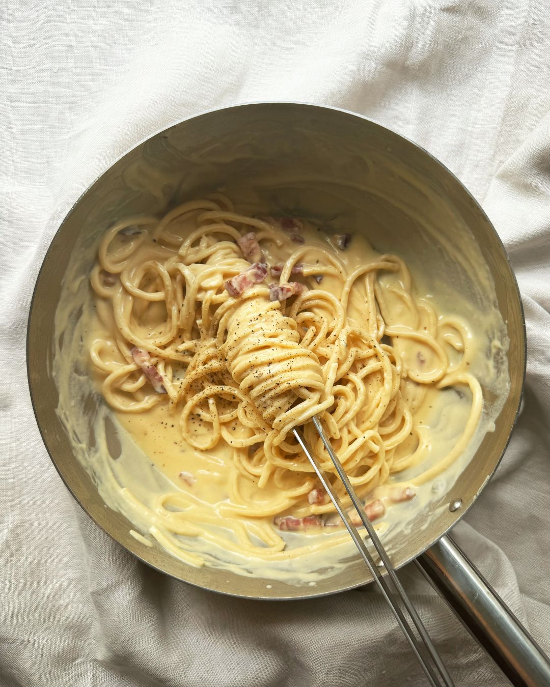 Pasta Carbonara with creamy sauce in a pan on a white cloth background
