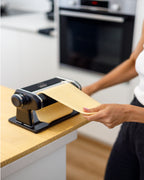 Person using a pasta machine on a kitchen counter 
