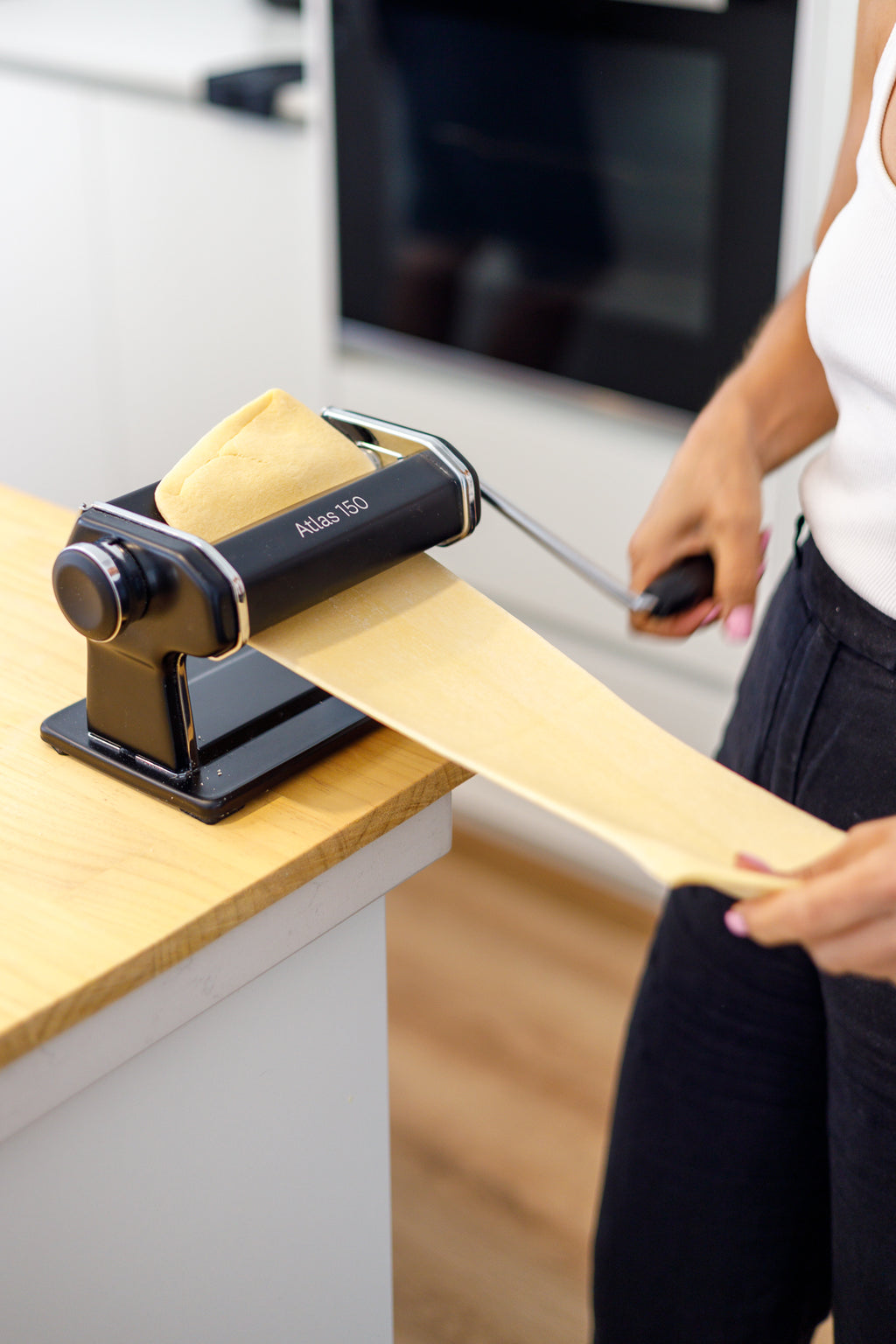 Person using a pasta machine to make pasta in a kitchen.