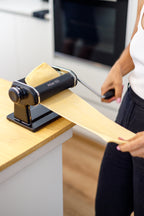 Person using a pasta machine to make pasta in a kitchen.
